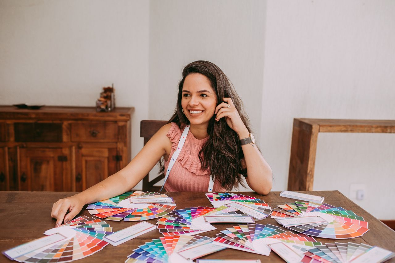 Smiling designer sitting at desk with various color palettes, showcasing creativity and design process.